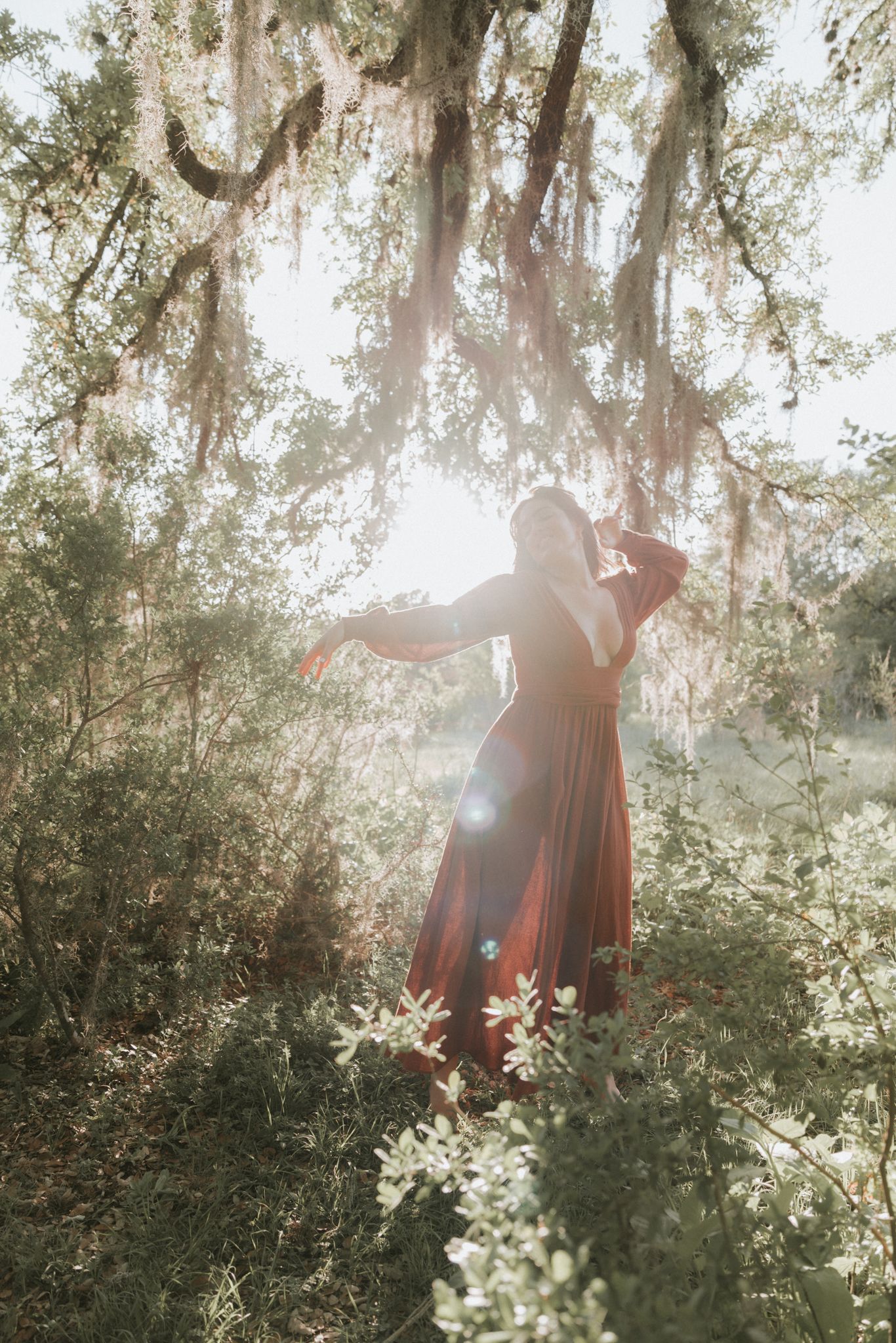 A woman dancing in a wine-red dress beneath Spanish moss
